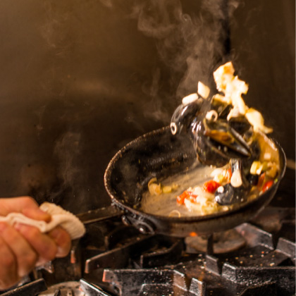 Action photo of CRU chefs cooking and flipping hot food in a skillet.